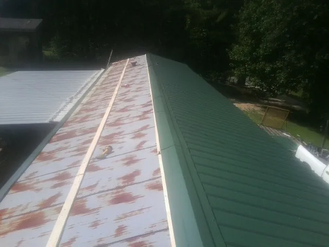 Old rusted panels beside newly installed green metal roofing — Wind Damage Roof Repair by Roofing Brothers in Magnolia