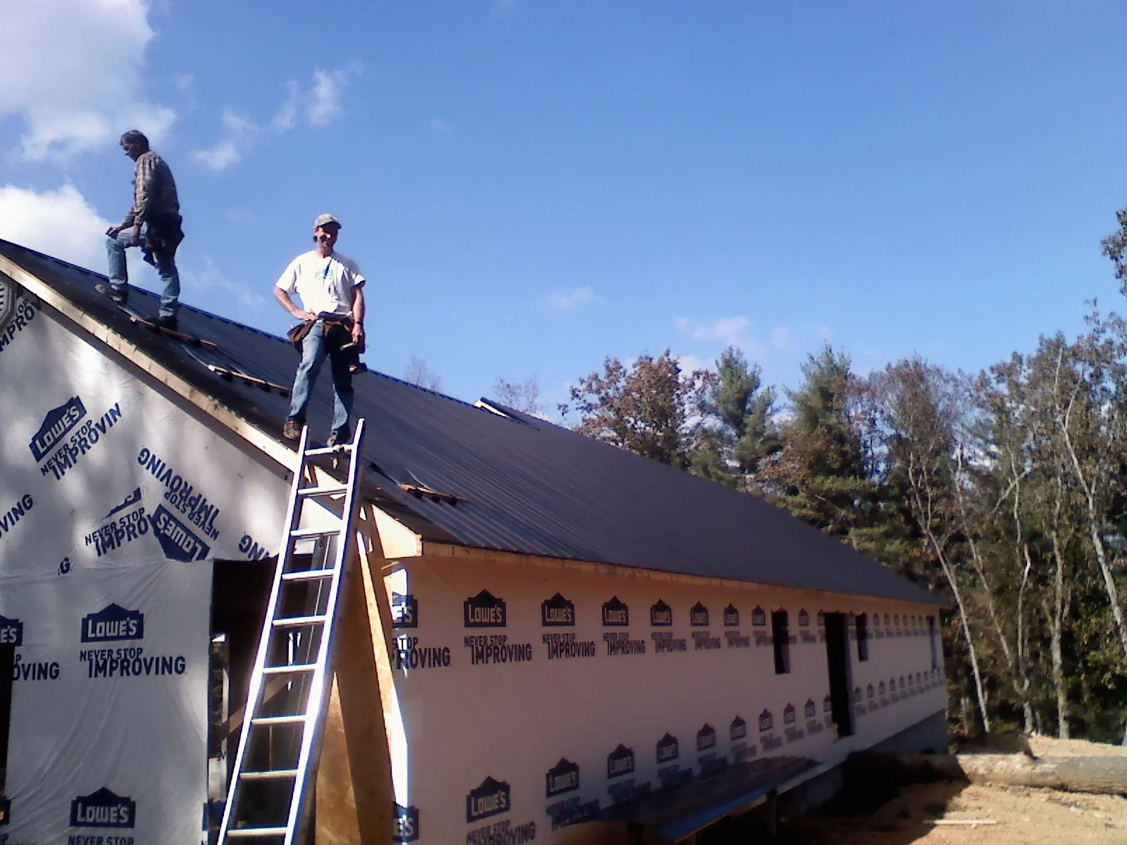Two roofers standing on a long dark metal roof over a wrapped building in Magnolia